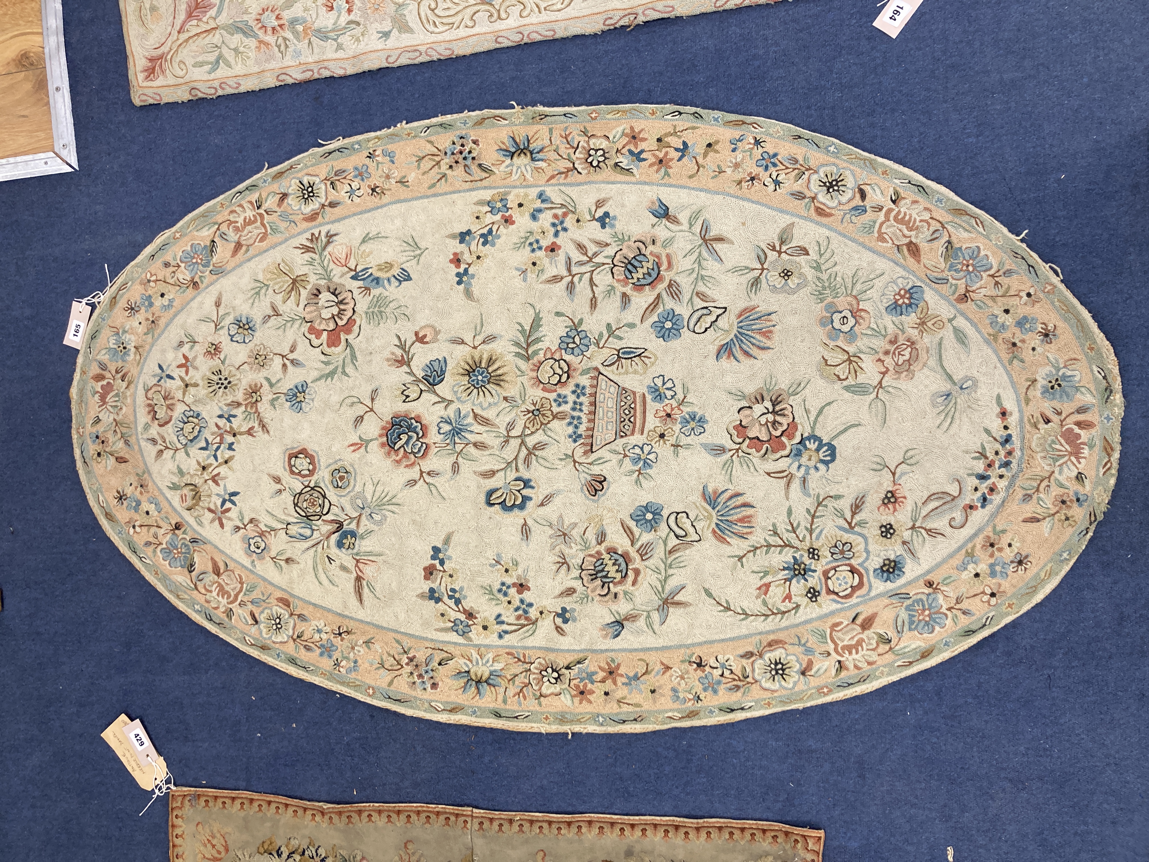 An Antique oval chain-stitch panel centred with flowers in a basket on a cream ground, 151 x 88cm